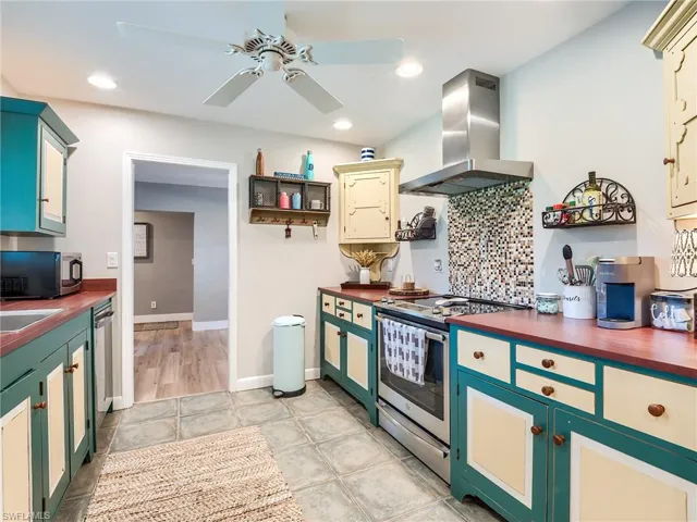 Kitchen featuring ceiling fan, stainless steel appliances, butcher block counters, light tile floors, and wall chimney range hood