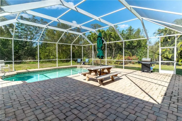 View of swimming pool with a grill, glass enclosure, and a patio area