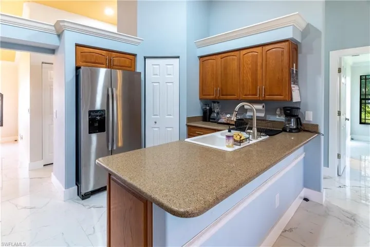 Kitchen with stainless steel refrigerator with ice dispenser, kitchen peninsula, sink, and a high ceiling