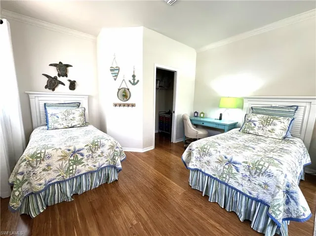 Guest Bedroom with ornamental molding, a closet, a walk in closet, and wood-type flooring
