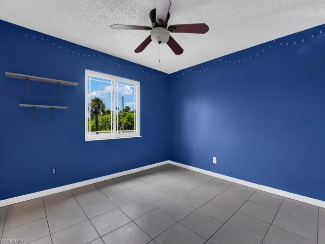 Tiled empty room with ceiling fan and a textured ceiling