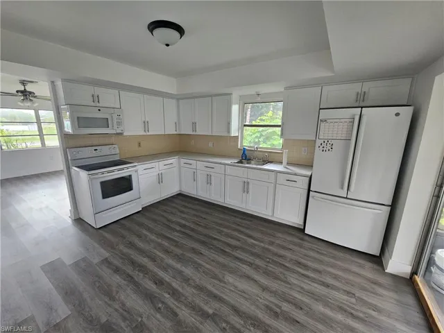 Kitchen with white appliances, light countertops, dark wood-style flooring, and tasteful backsplash