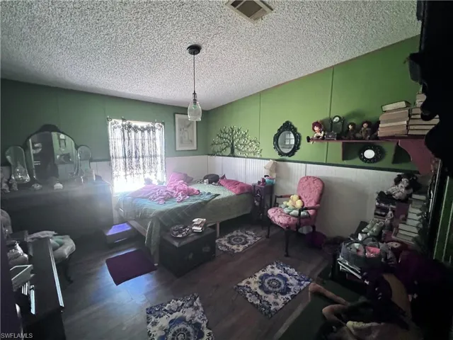 Bedroom with a textured ceiling, wainscoting, and wood finished floors