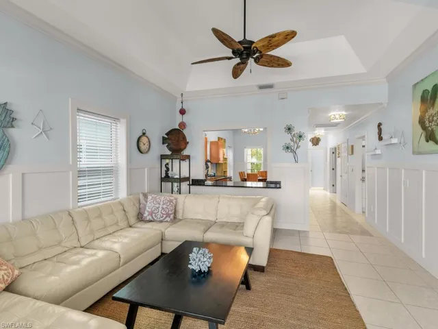 Living room featuring crown molding, a raised ceiling, wainscoting, a decorative wall, and light tile patterned floors