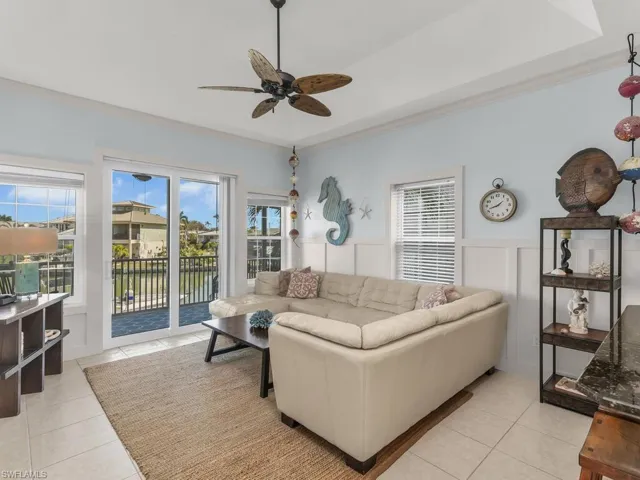 Living room featuring a tray ceiling, light tile patterned floors, ceiling fan, ornamental molding, and a decorative wall