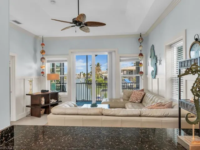 Living room featuring ornamental molding, a wainscoted wall, a ceiling fan, a water view, and a decorative wall