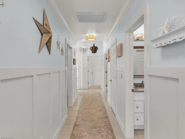 Hallway featuring crown molding, light tile patterned flooring, a chandelier, and a decorative wall