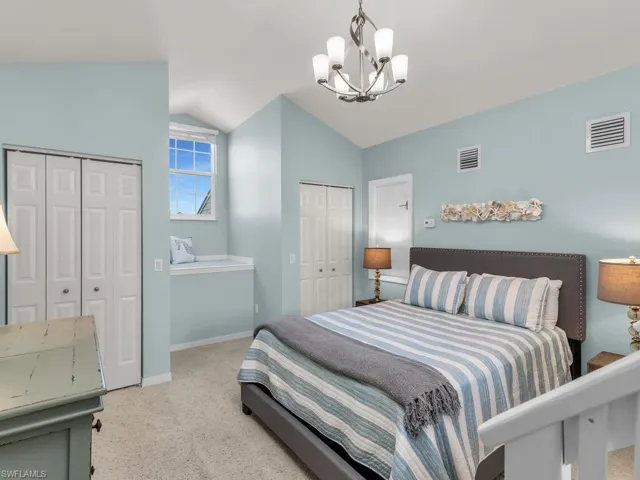 Bedroom featuring lofted ceiling, multiple closets, light colored carpet, and a chandelier