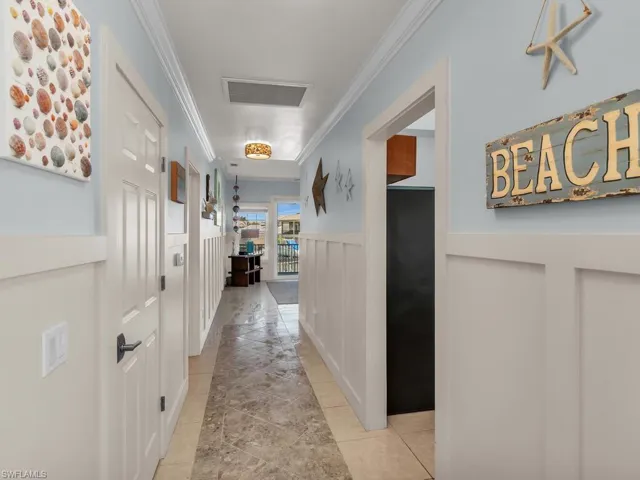 Hallway with crown molding, wainscoting, light tile patterned floors, and a decorative wall