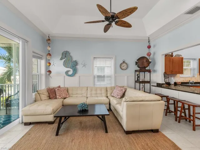 Living area with light tile patterned flooring, wainscoting, ceiling fan, a tray ceiling, and a decorative wall