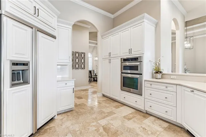 Kitchen featuring pendant lighting, stainless steel double oven, crown molding, paneled fridge, and white cabinetry