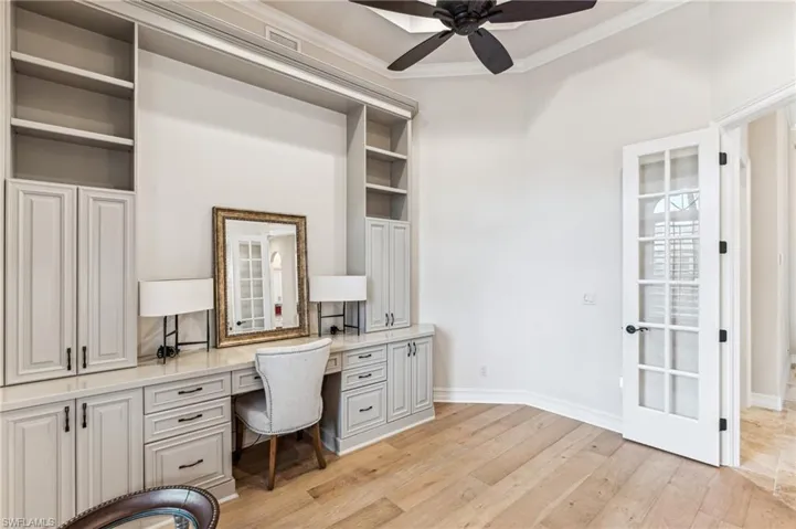 Office area with built in desk, ceiling fan, light wood-type flooring, and crown molding