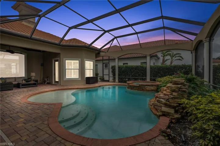 Pool at dusk featuring glass enclosure, a patio, and an in ground hot tub