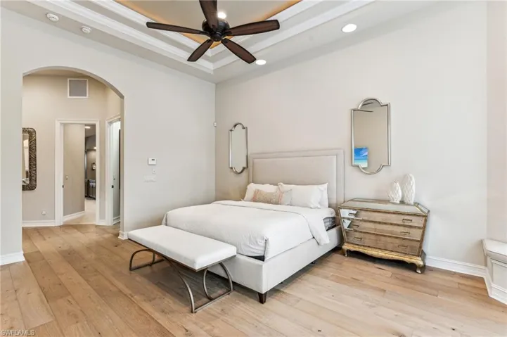Bedroom with ceiling fan, a raised ceiling, crown molding, and wood-type flooring