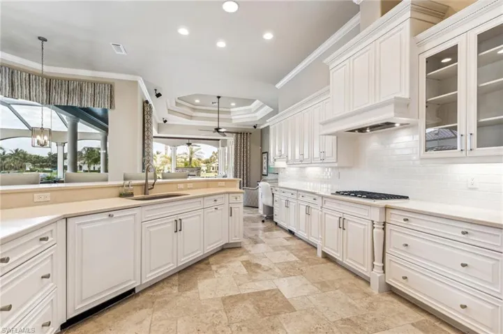 Kitchen with white cabinets, sink, tasteful backsplash, ornamental molding, and decorative light fixtures