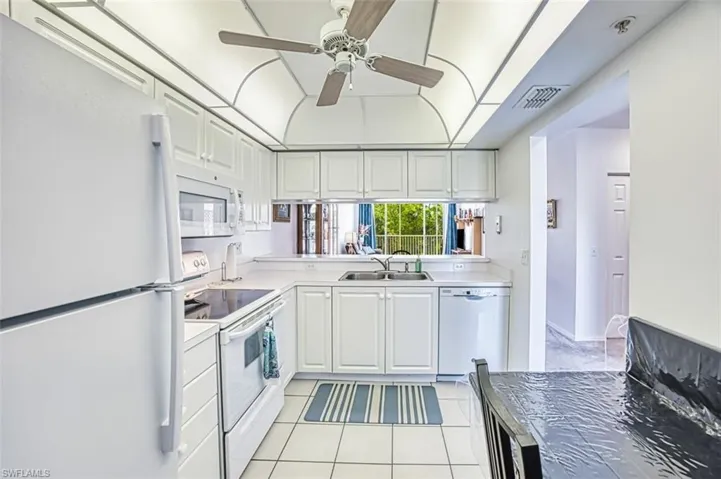 Kitchen with visible vents, a sink, light tile patterned flooring, white appliances, and ceiling fan