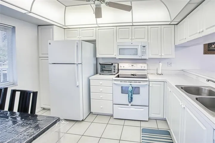 Kitchen with white cabinets, light tile patterned flooring, a sink, and white appliances