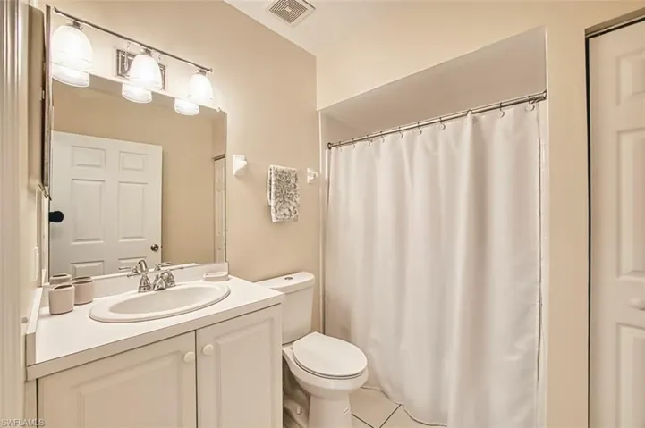 Full bathroom with tile patterned floors, toilet, visible vents, curtained shower, and vanity