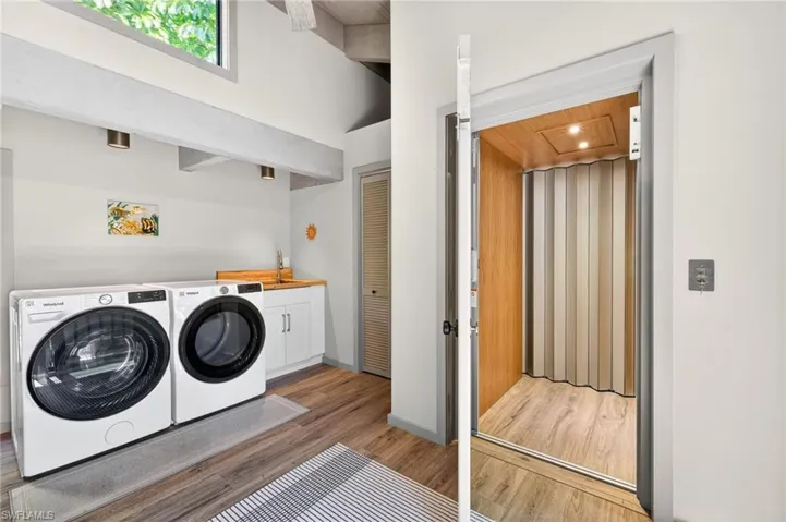 Laundry area featuring light wood-style floors, washer and dryer, elevator, wood ceiling, and cabinet space