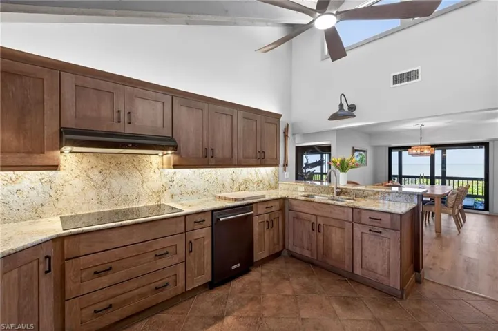 Kitchen featuring a peninsula, light stone countertops, a ceiling fan, decorative backsplash, and black appliances