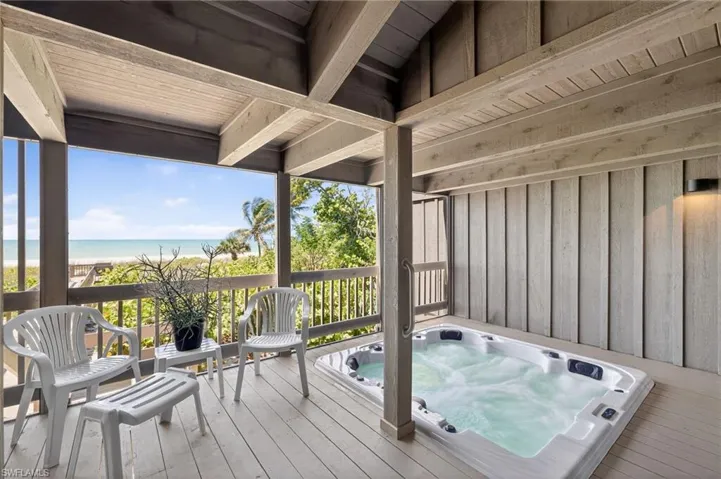 Sunroom featuring view of water and beach with hot tub