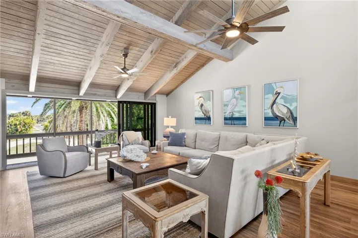 Living room with a ceiling fan, wood finished floors, and a high wooden beamed ceiling