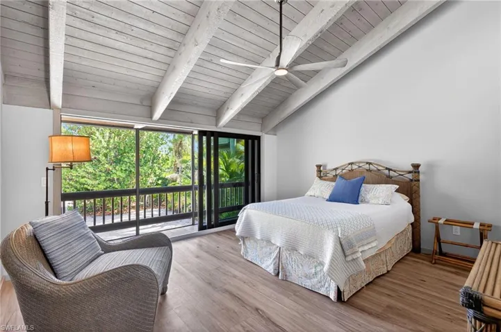 Bedroom featuring lofted ceiling with beams, access to outside, wood finished floors, and multiple windows