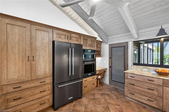 Kitchen with high quality fridge, ceiling fan, wood ceiling, light stone counters, and vaulted ceiling with beams