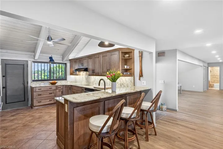 Kitchen featuring a breakfast bar area, open shelves, lofted ceiling with beams, light stone countertops, and backsplash
