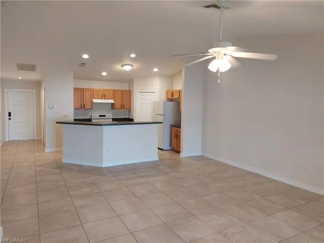 Kitchen with dark countertops, white appliances, open floor plan, a ceiling fan, and light tile patterned floors