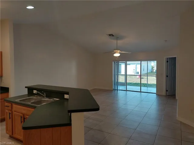Kitchen with dark countertops, wood finish cabinets, light tile patterned floors, lofted ceiling, and recessed lighting