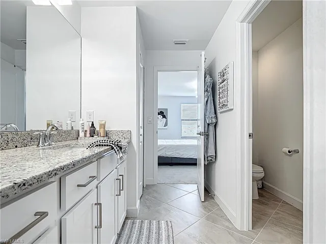 Bathroom with visible vents, vanity, toilet, baseboards, and connected bathroom
