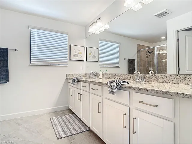 Full bath featuring a sink, double vanity, baseboards, a shower stall, and visible vents