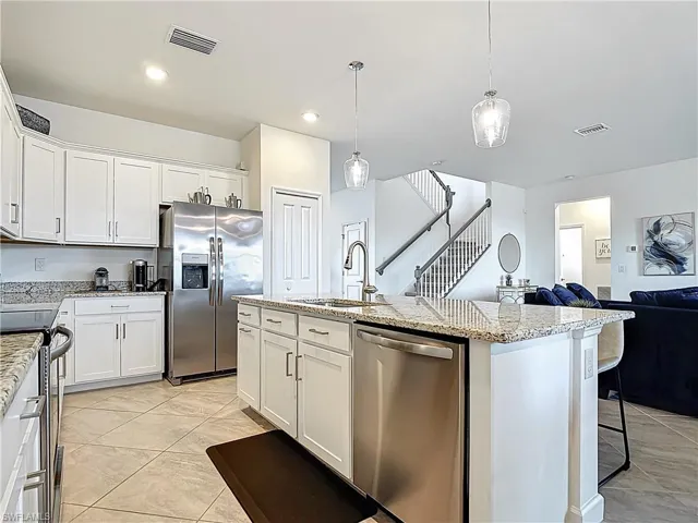 Kitchen with a sink, appliances with stainless steel finishes, light stone counters, and visible vents
