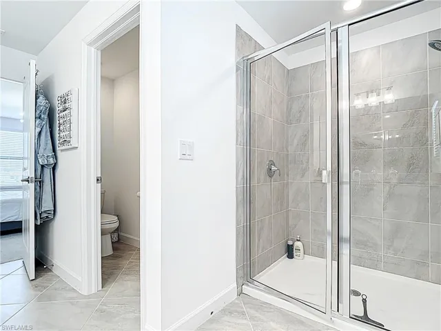 Bathroom featuring toilet, baseboards, marble finish floor, and a stall shower