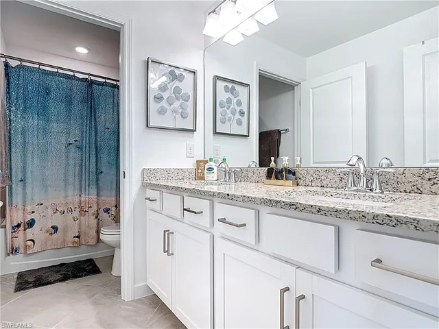 Bathroom with a sink, tile patterned flooring, double vanity, toilet, and shower / bath combo with shower curtain