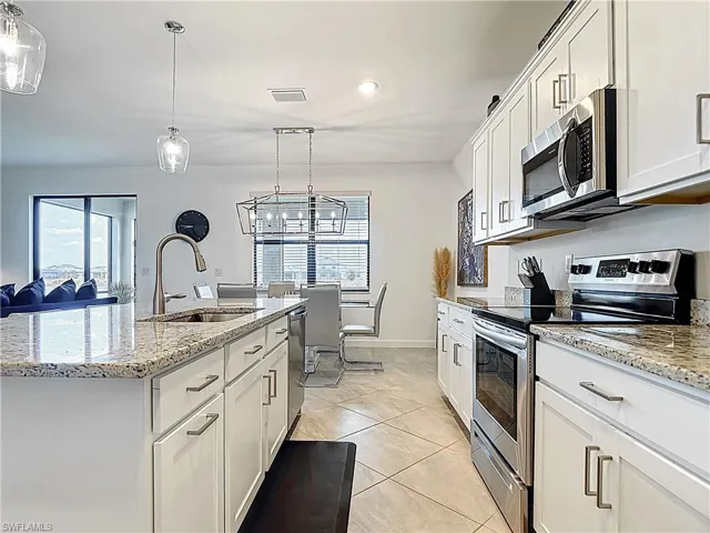 Kitchen featuring appliances with stainless steel finishes, light stone counters, a sink, white cabinetry, and visible vents
