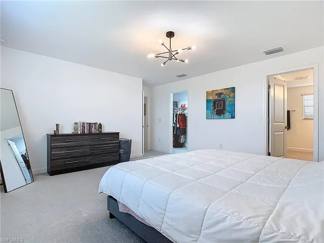 Bedroom with visible vents, an inviting chandelier, baseboards, a walk in closet, and light colored carpet