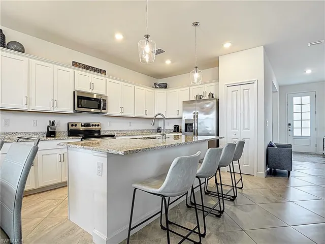 Kitchen with white cabinets, light stone counters, a sink, stainless steel appliances, and a center island with sink