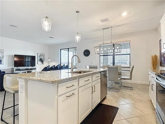 Kitchen featuring a kitchen island with sink, light tile patterned flooring, light stone countertops, open floor plan, and a sink