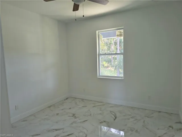 White interior walls, wood-finish ceiling fan, white window trim, and marble-look tile flooring