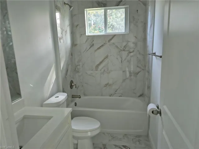 Bathroom featuring a built-in tub with shower, tiled surround, window, and single vanity with an integrated sink
