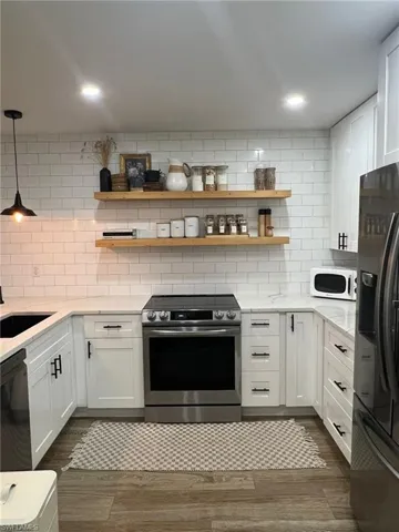 Kitchen featuring a stainless steel electric range, white shaker-style cabinetry with black hardware, and light-toned countertops