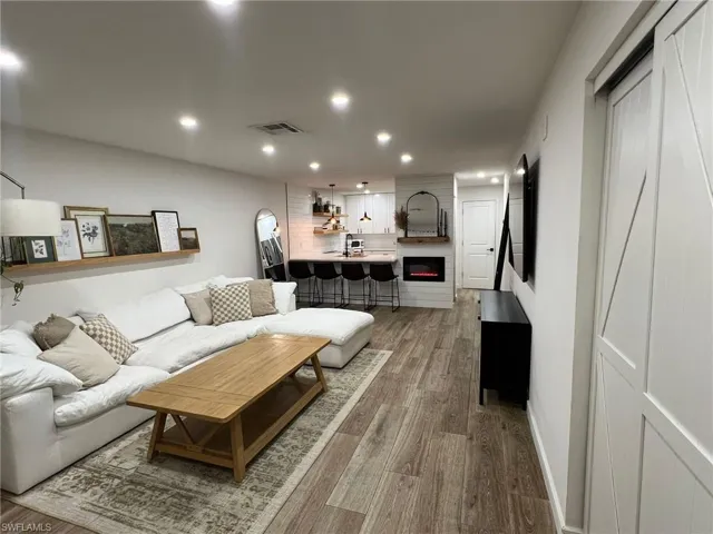 Open-concept living space featuring wood-finish flooring, recessed lighting, a modern electric fireplace with a shiplap surround, and a kitchen island with seating