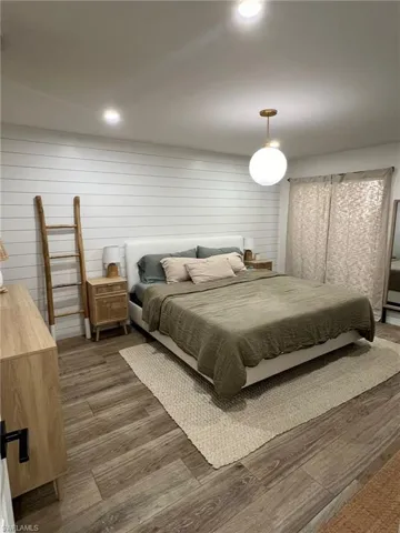 Spacious bedroom featuring wood-finish flooring, a white shiplap accent wall, recessed lighting, and a contemporary globe pendant light fixture