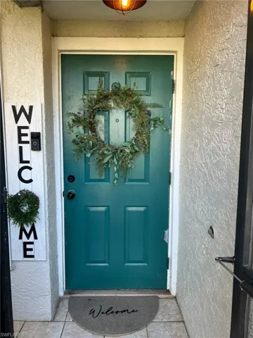Entryway featuring a teal paneled door with black hardware, textured stucco siding, and tiled flooring