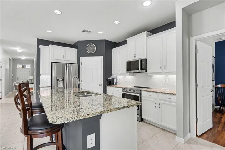Kitchen with stainless steel appliances, light stone countertops, white cabinets, a breakfast bar, and recessed lighting