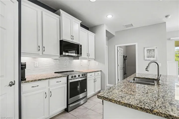 Kitchen with stainless steel appliances, white cabinetry, light stone counters, light tile patterned floors, and decorative backsplash