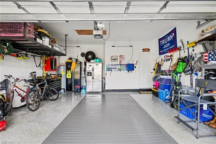 Garage featuring stainless steel fridge with ice dispenser, water heater, a garage door opener, and freestanding refrigerator