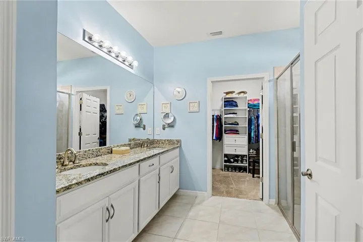 Full bath with a stall shower, double vanity, a walk in closet, and light tile patterned floors